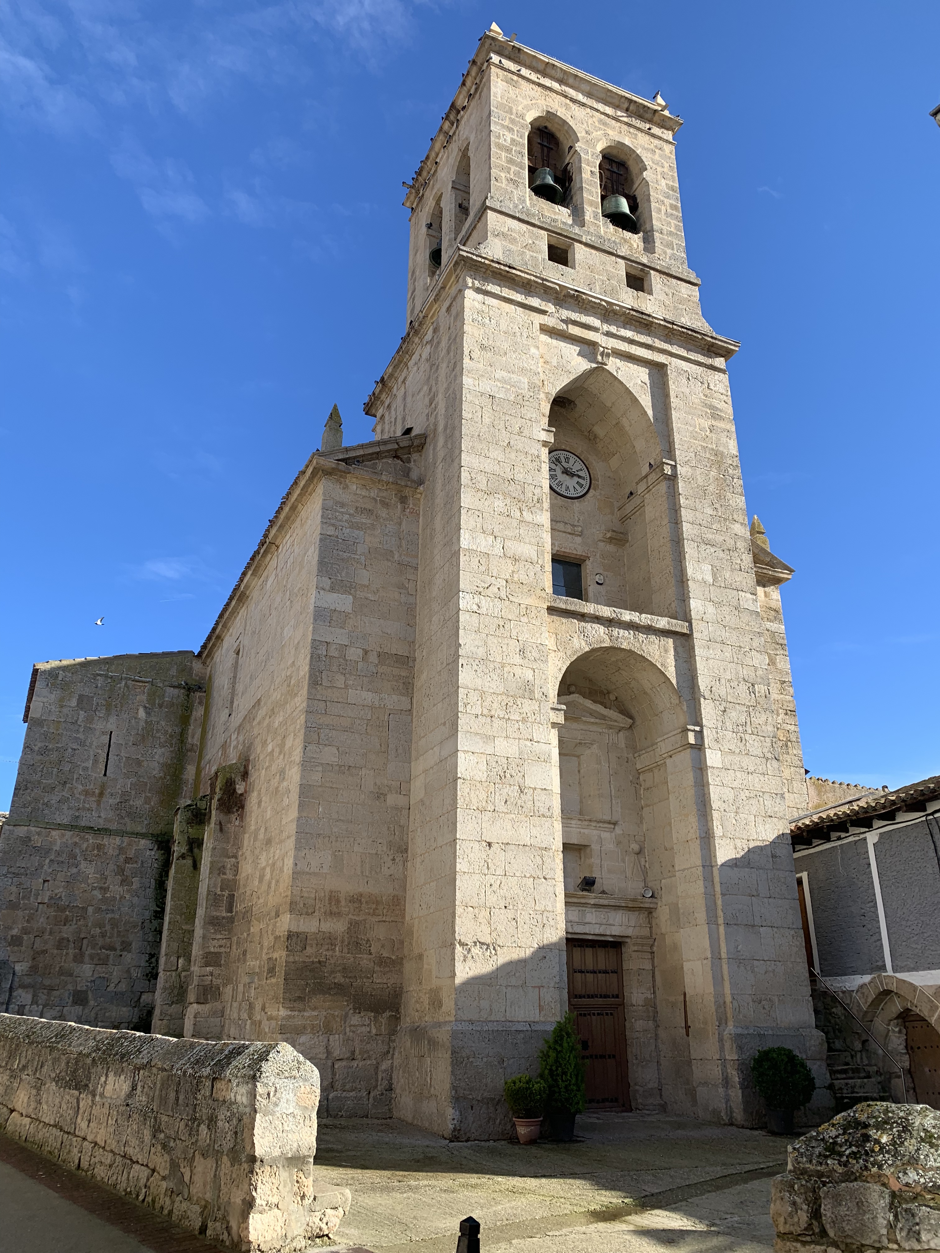 Stone church tower with a clock, bell towers, and clear blue sky in the background.
